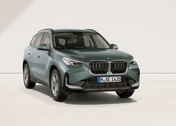 Graugrüner BMW X1 in Front-Seitenansicht vor hellem Hintergrund.