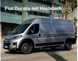 Die Seitenansicht zeigt einen silberfarbenen Fiat Ducato Kastenwagen in der Hochdach-Ausführung. Das moderne Nutzfahrzeug hat unlackierte, schwarze Kunststoffteile an den Radläufen und der unteren Frontschürze. Es steht auf einer städtischen Straße vor einem modernen Bürogebäude mit blauen Glasfassaden und hohen Palmen im Hintergrund.