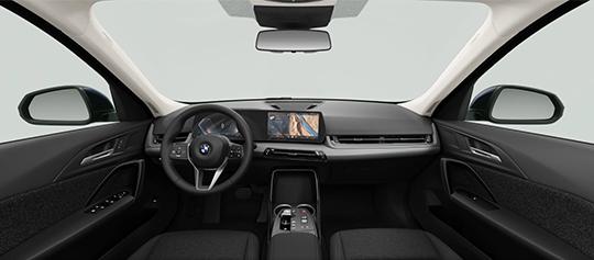  Eine Aufnahme des Innenraums des BMW X1, die die Fahrerkabine aus der Mitte der Rückbank zeigt. Das Armaturenbrett mit dem Curved Display, das Lenkrad und die schwebende Mittelkonsole sind sichtbar. Die Ausstattung wirkt modern und schlicht in dunklen Farben gehalten.