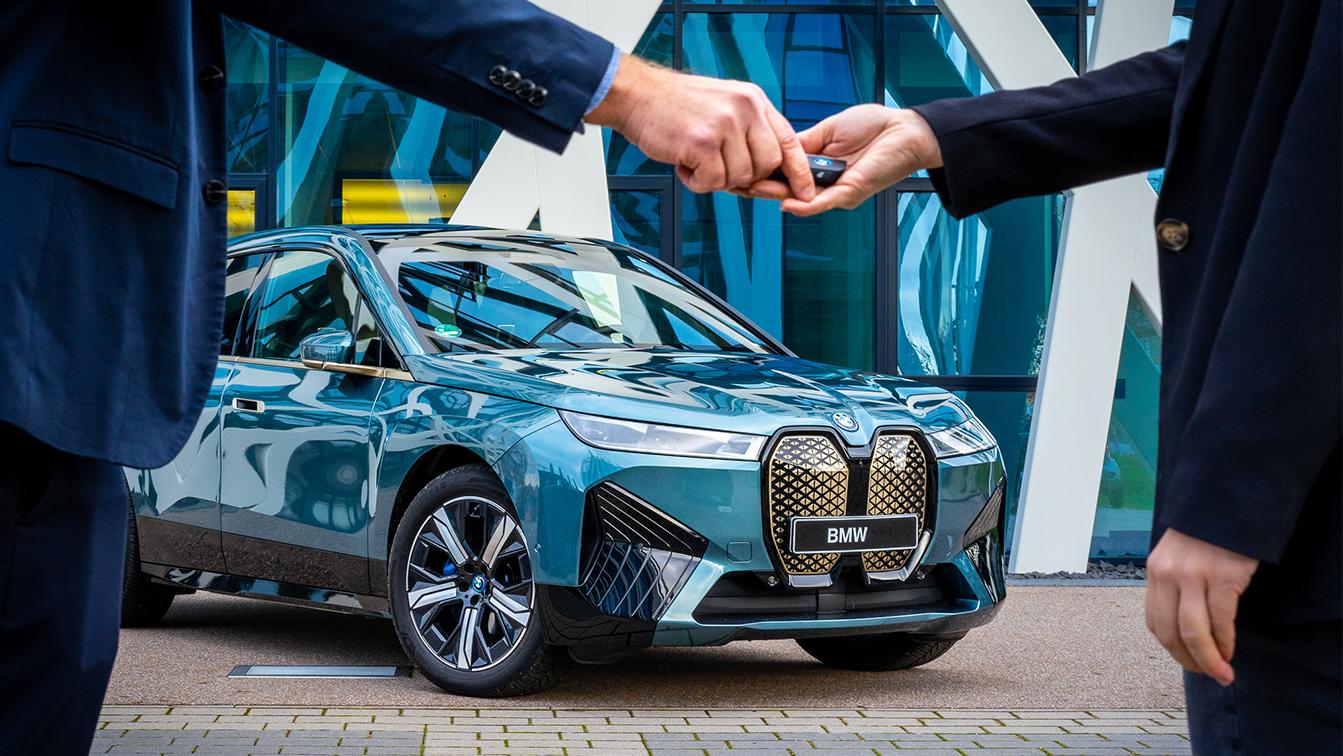 Übergabe eines Fahrzeugschlüssels vor einem BMW iX als Symbol für die Fahrzeugvermietung.